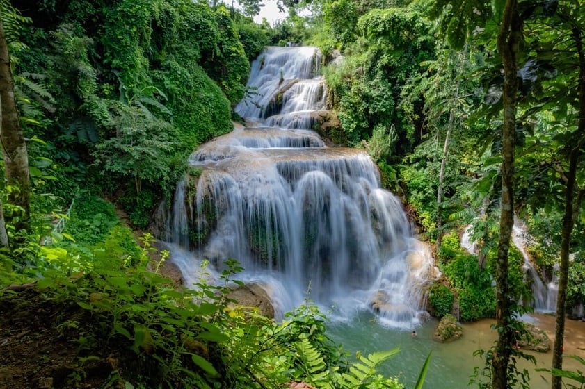 A view of the multiple tiers of Mu Waterfall cascading through dense foliage.